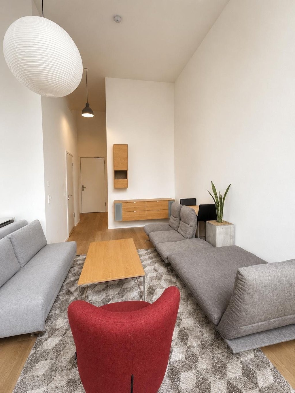 Wohnzimmer mit weißen Wänden und Decke, grauen Sofas, rotem Sessel und großer Papierleuchte