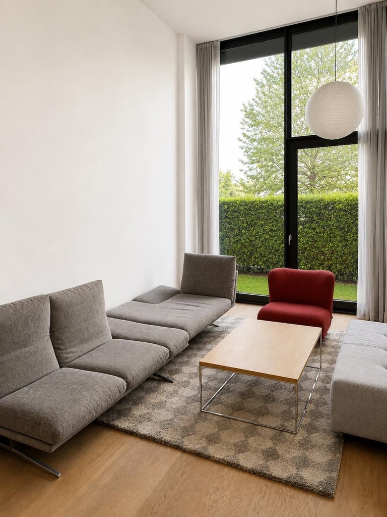Wohnraum mit grauem Sofa, rotem Sessel, Holz-Couchtisch und großer Fensterfront zum Garten, dahinter weiße Wand